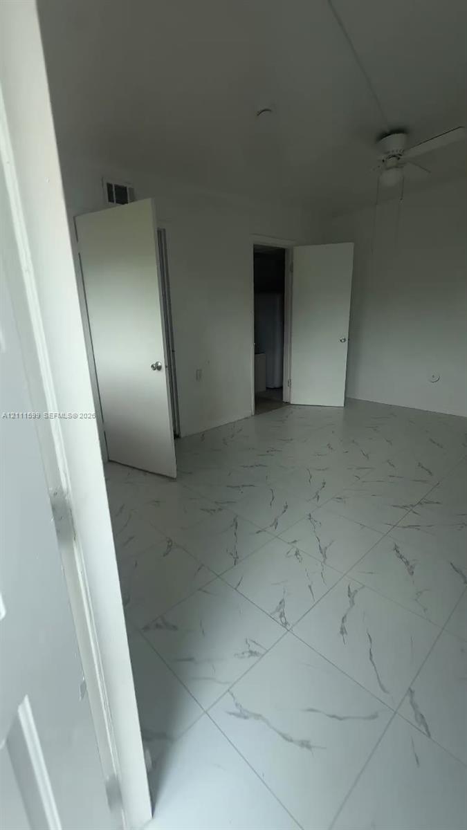 Large-format tile flooring with a white finish and grey veining, ceiling fan with integrated lighting, and white interior doors