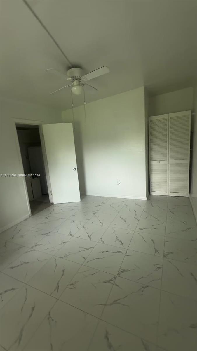 Large-format tile flooring with veining detail, ceiling-mounted paddle fan, and bi-fold louvered closet doors