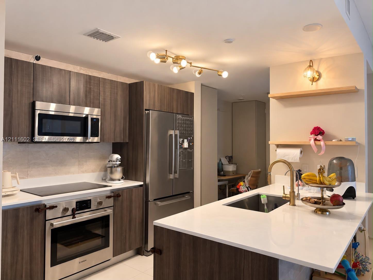 Kitchen featuring flat-panel wood-finish cabinetry, quartz countertops, stainless steel appliances, a multi-light brass fixture, and floating wooden shelving