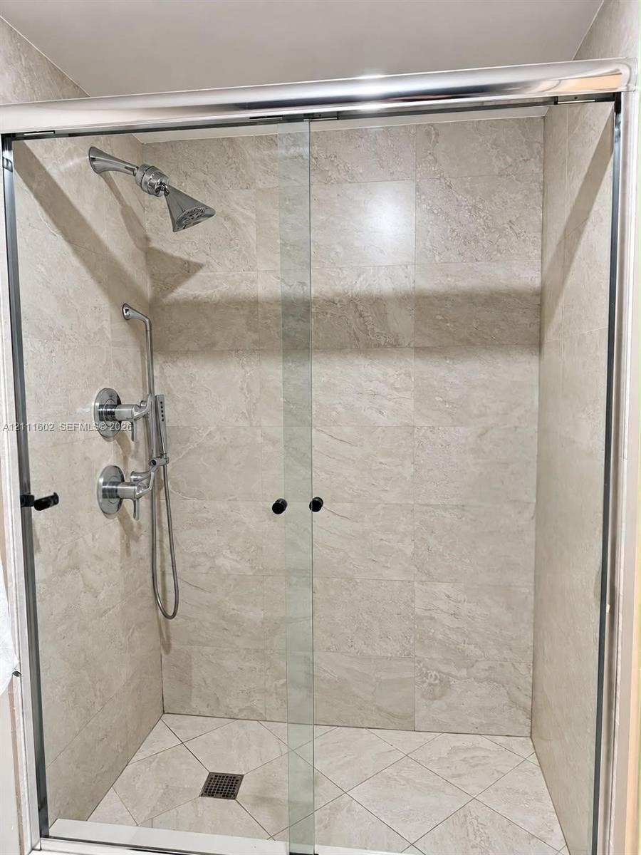 Walk-in shower featuring floor-to-ceiling stone-finish tile surround, sliding glass enclosure, polished chrome shower head, handheld sprayer, and diagonal-patterned floor tile