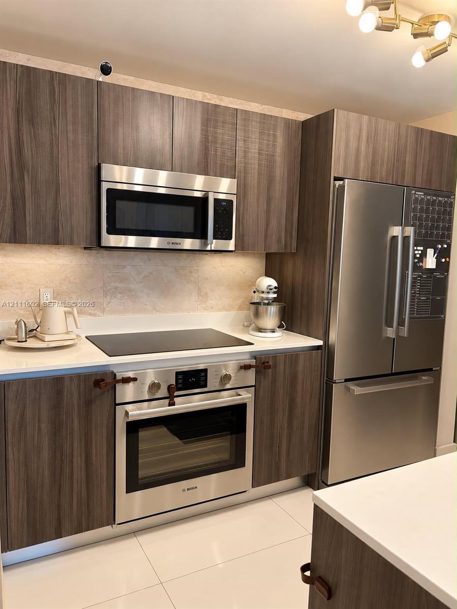 Kitchen featuring wood-finish cabinetry, stainless steel Bosch appliances, solid surface countertops, a stone-tile backsplash, and polished tile flooring