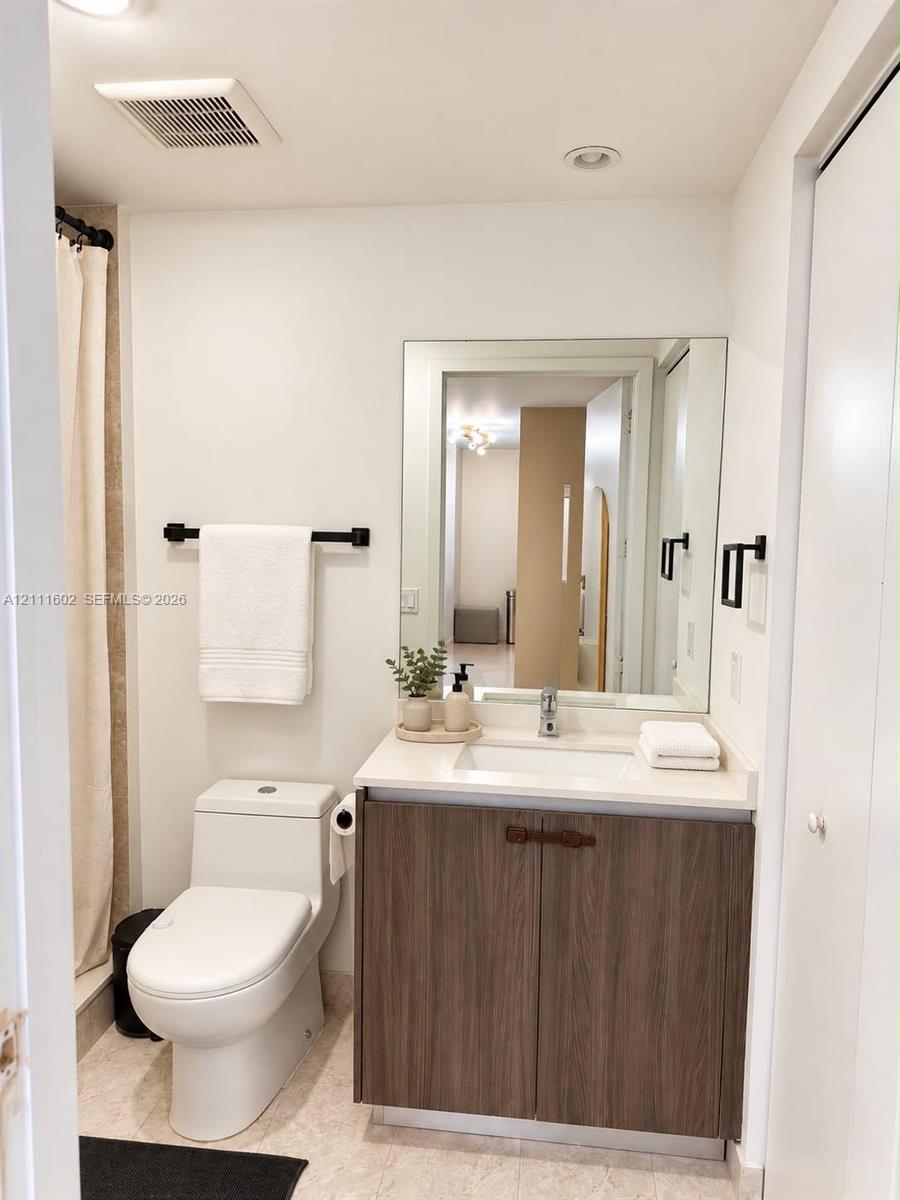 Bathroom featuring a vanity with a wood-finish cabinet, solid surface countertop, integrated rectangular sink, wall-mounted mirror, and matte black hardware