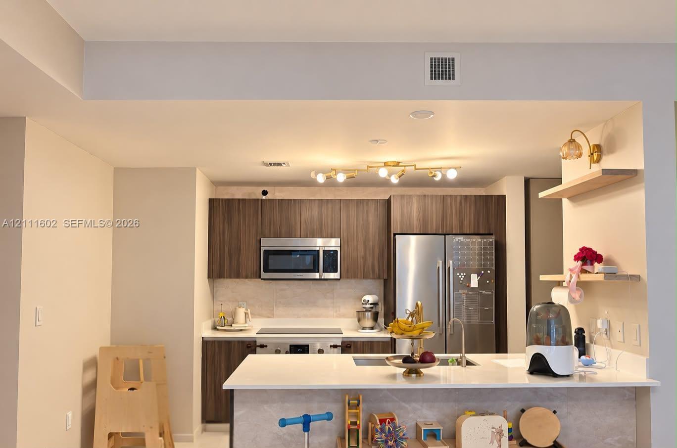 Kitchen featuring dark wood-finish cabinetry, stainless steel appliances, quartz countertops, a central island, and modern multi-bulb overhead lighting