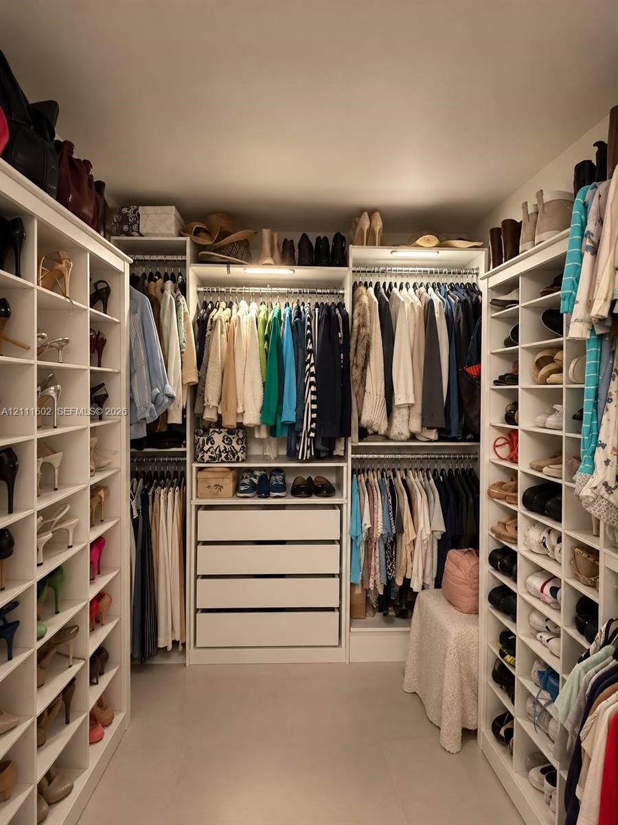 Walk-in closet featuring extensive built-in white shelving, multiple hanging rods, four deep storage drawers, and integrated overhead lighting
