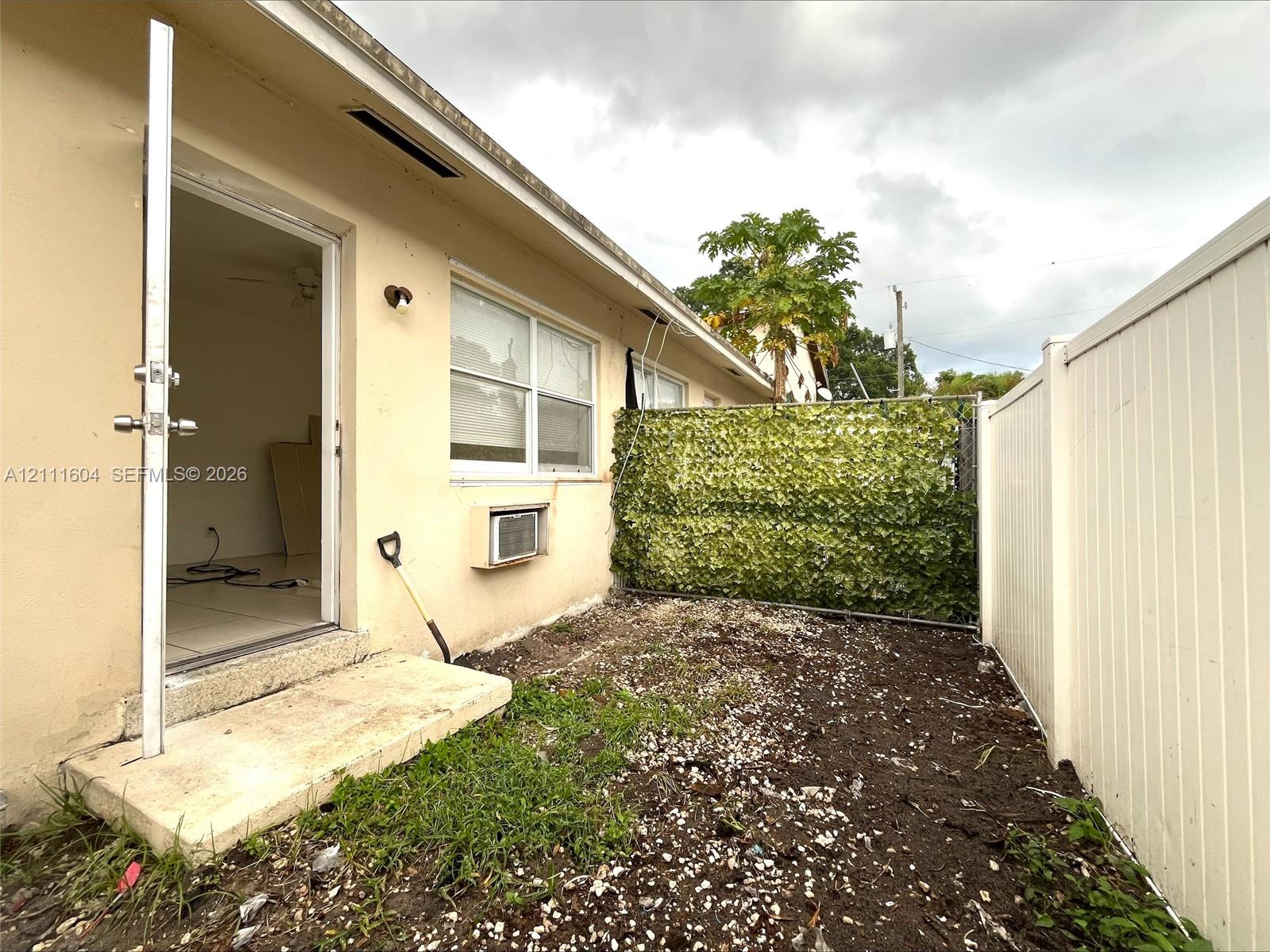 Exterior space featuring a concrete step, white vinyl privacy fencing, and a decorative foliage screen