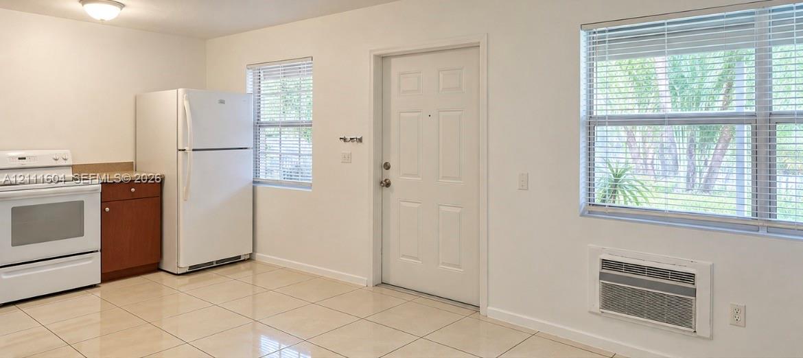 Kitchen space featuring ceramic tile flooring, neutral wall finishes, windows with horizontal blinds, built-in cabinetry, and a wall-mounted air conditioning unit