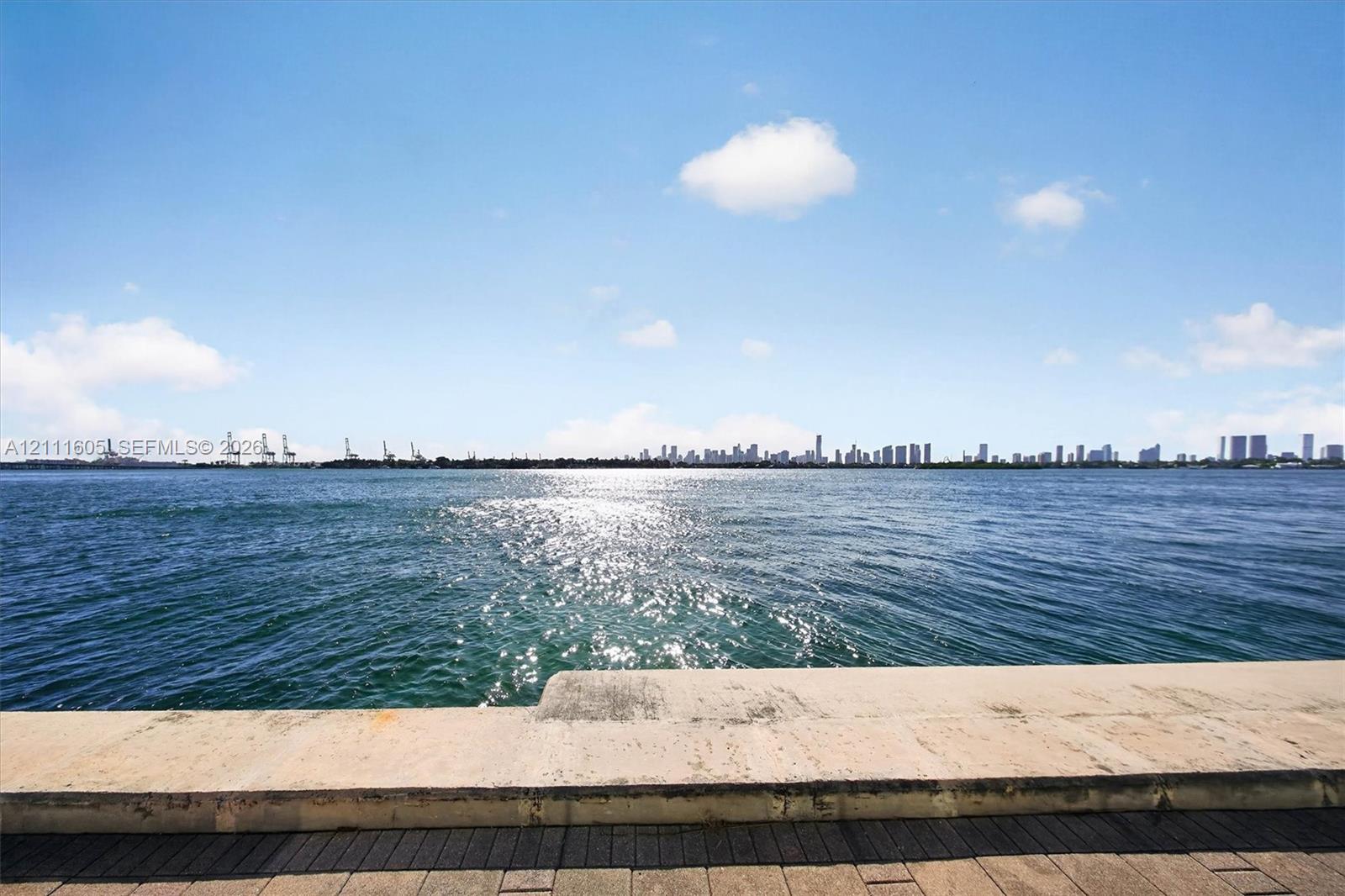 High-rise residential exterior featuring a waterfront swimming pool, manicured landscaping, palm trees, and paved patio area