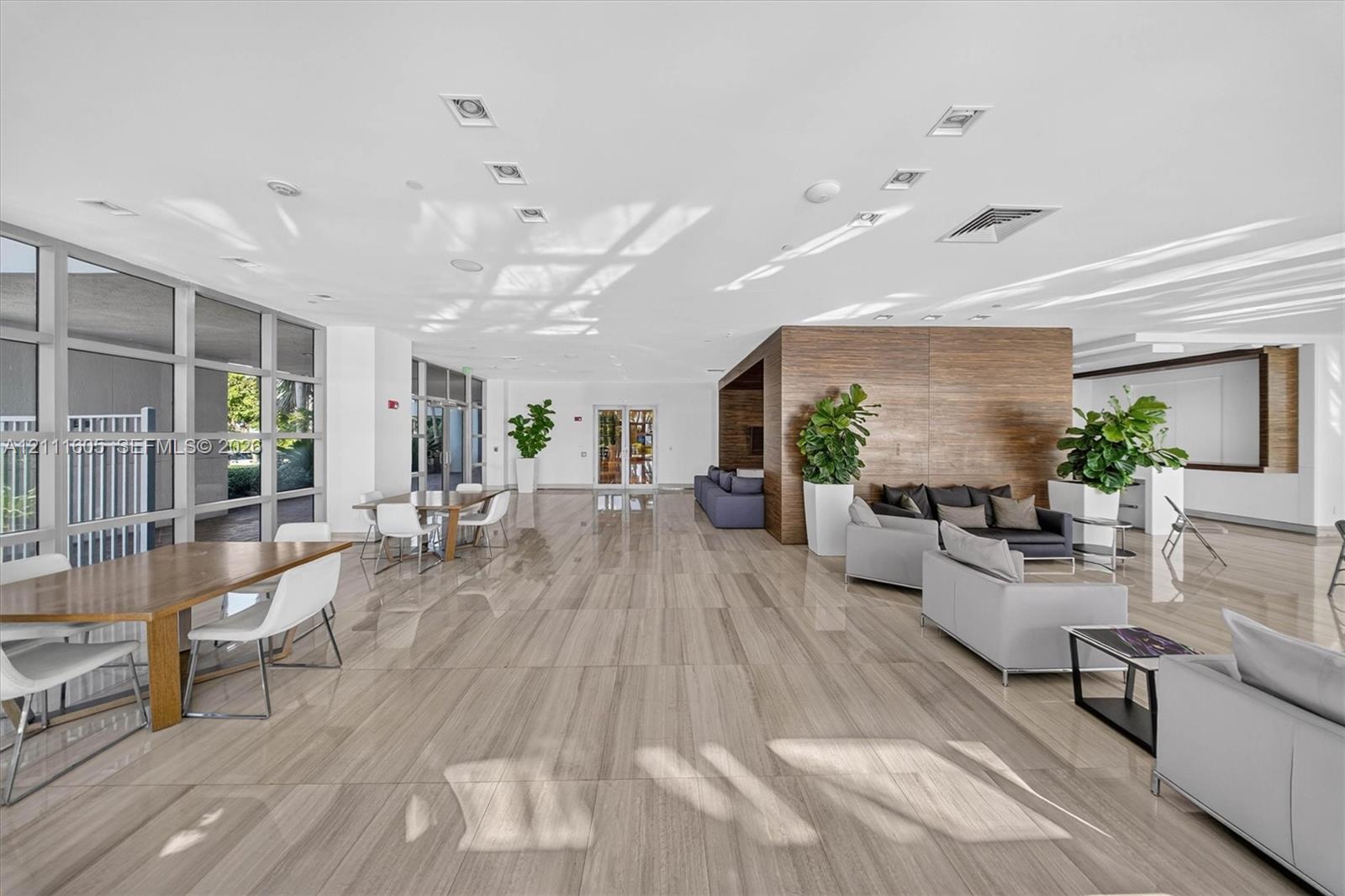 Spacious communal area featuring large-format stone-finish flooring, full-height glass window panels, and a prominent wood-panel accent wall with integrated recessed lighting
