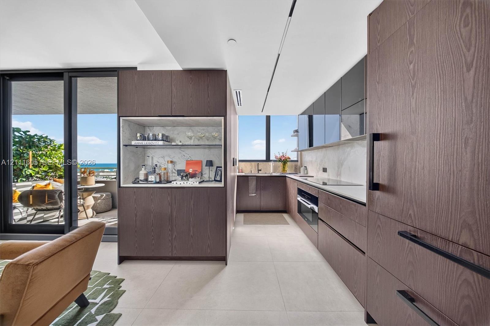 Kitchen featuring flat-panel wood-finish cabinetry, integrated appliances, stone backsplash, built-in dry bar, and large-format tile flooring