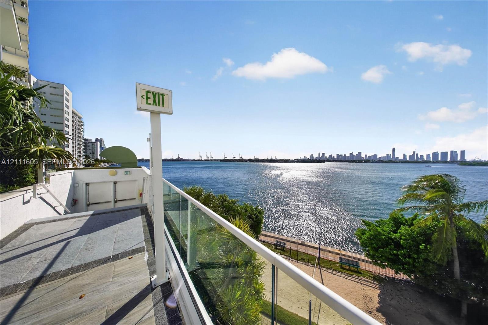 Waterfront terrace featuring large-format stone tiling and glass panel railing overlooking the bay and skyline