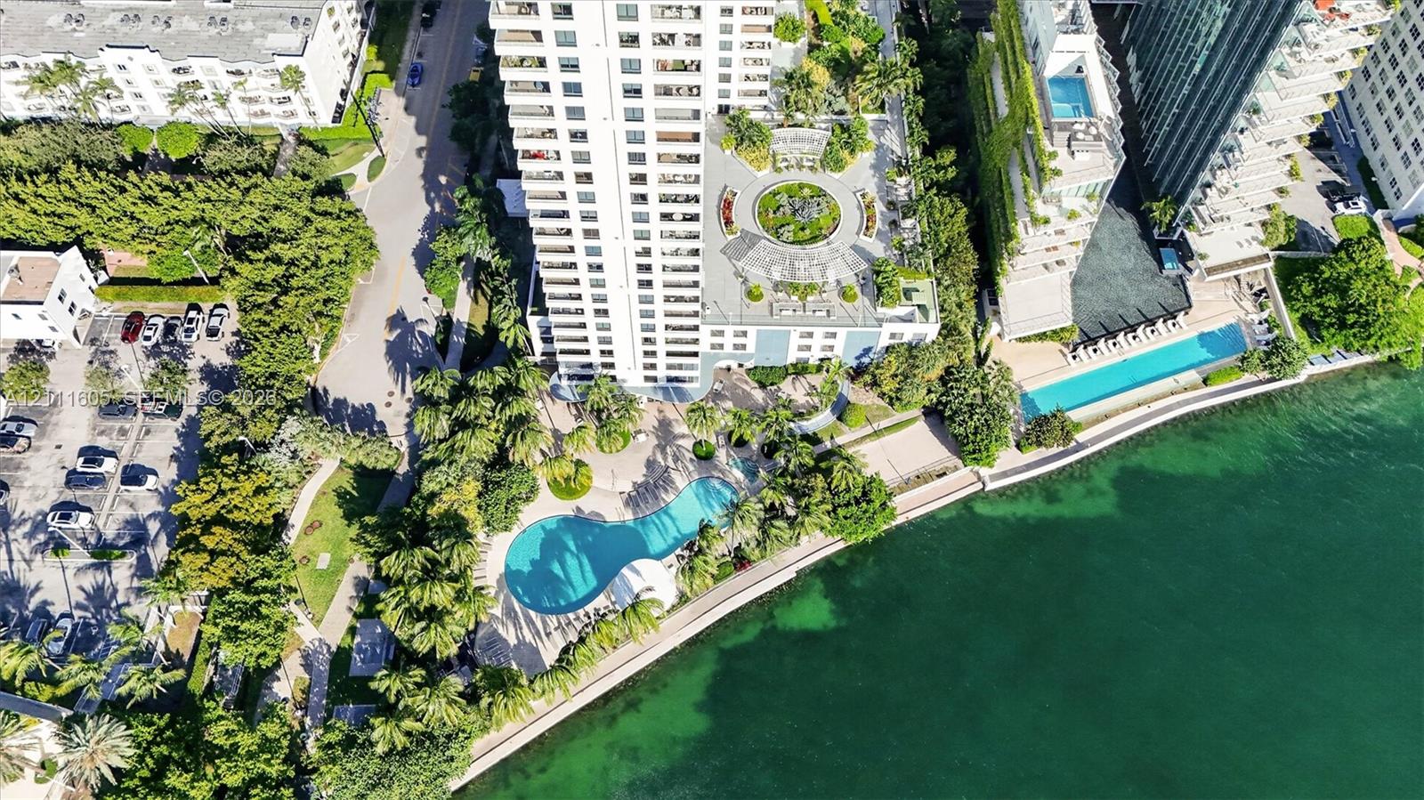 High-rise residential exterior with multi-level private balconies, waterfront swimming pool, manicured grounds featuring mature palm trees, and hardscaped patio areas