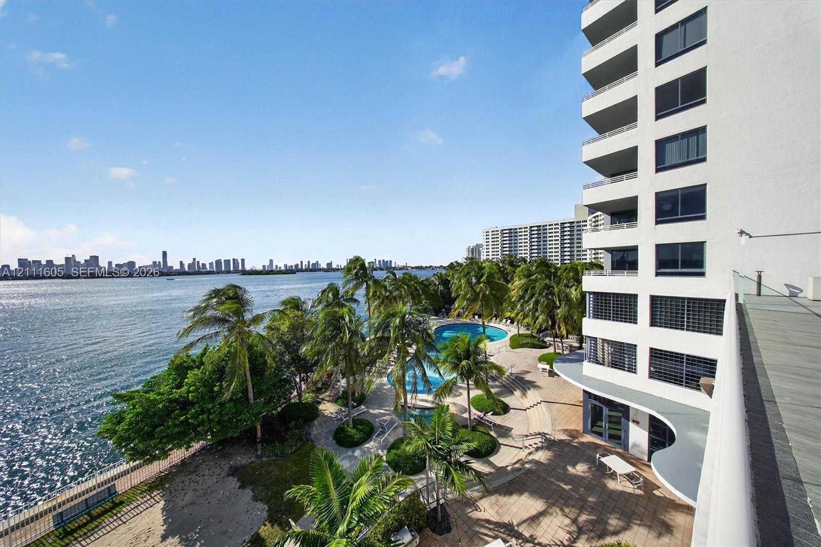 High-rise residential tower featuring a white facade, private balconies, a clock tower element, and waterfront positioning