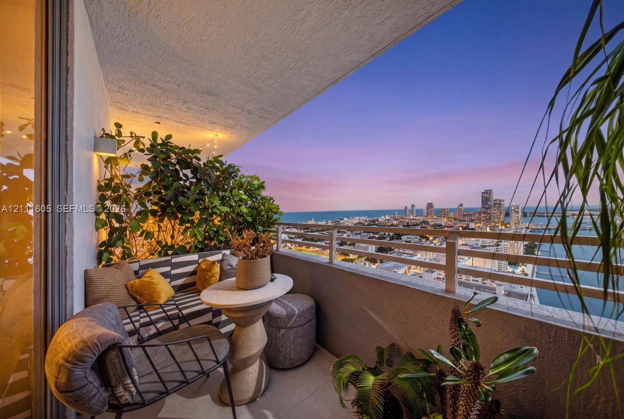 Covered balcony featuring concrete flooring, a horizontal metal railing, and an expansive cityscape and water horizon backdrop