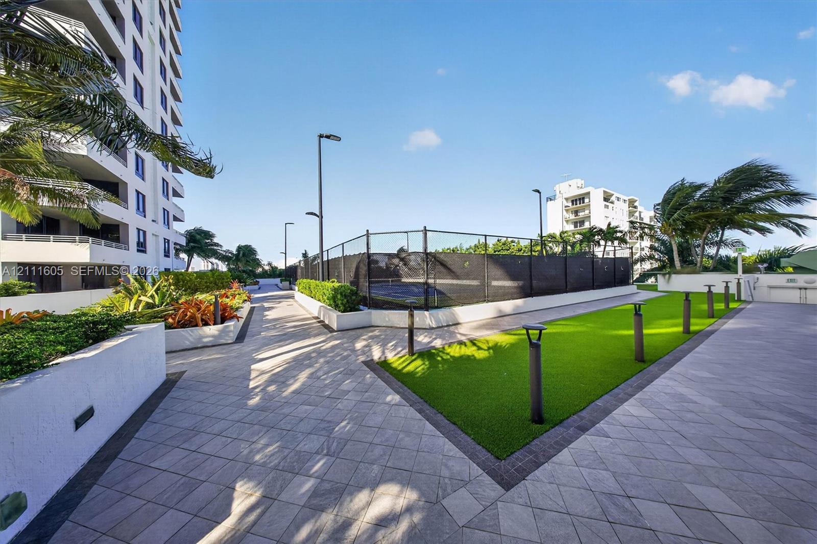 Aerial perspective of a high-rise residential building featuring a landscaped podium terrace with a circular water feature, a kidney-shaped ground-level swimming pool, and direct proximity to the waterfront