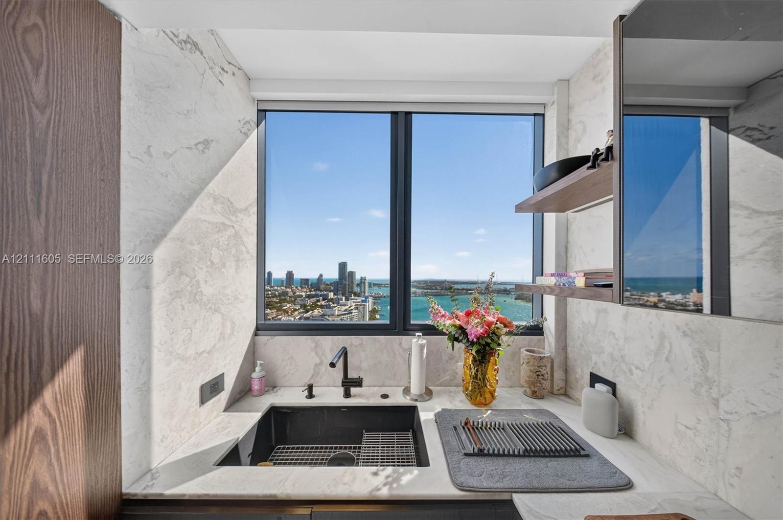 Stone countertop, undermount sink, matte black hardware, stone-finish wall cladding, and wood-finish cabinetry