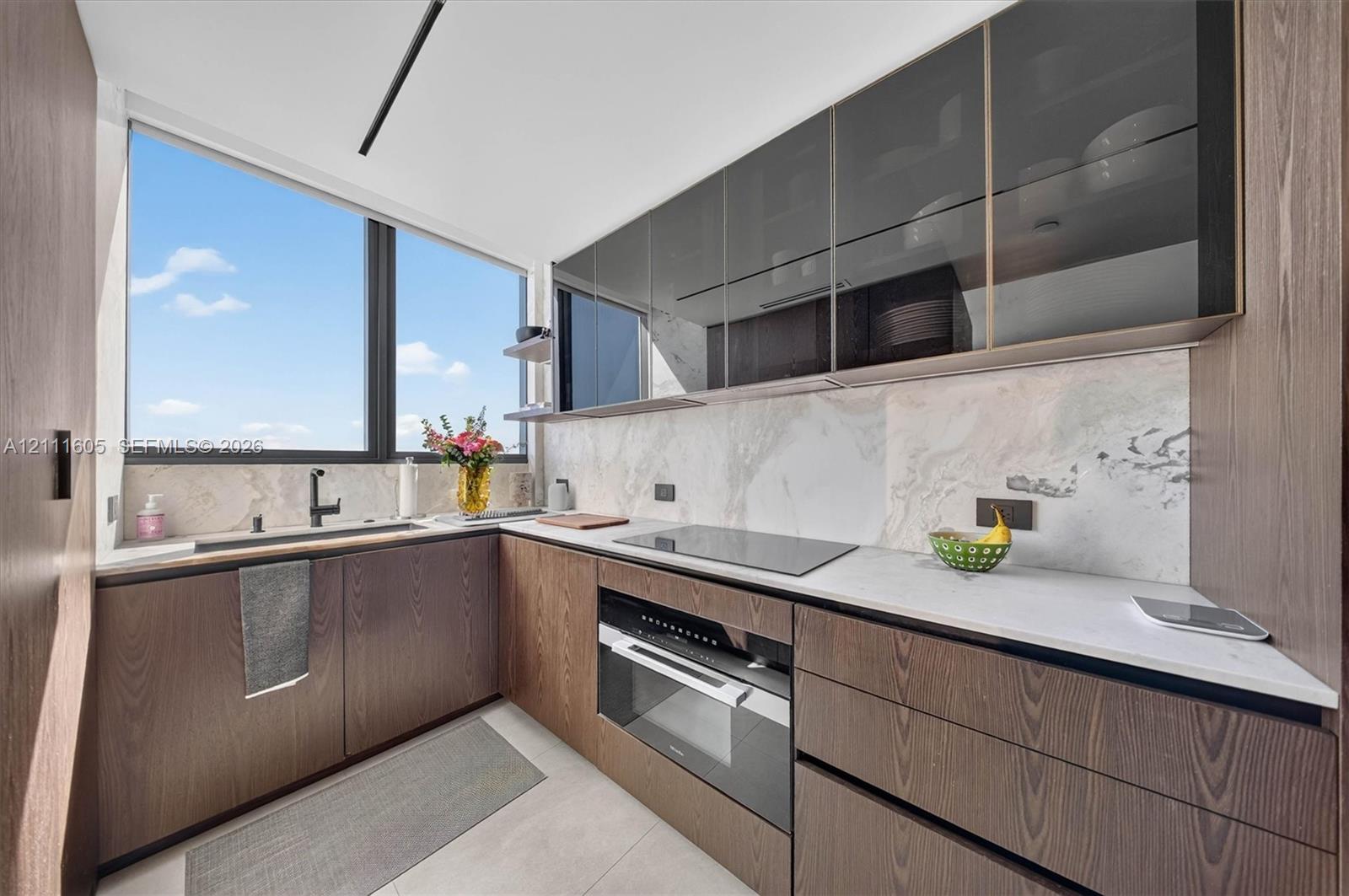 Kitchen featuring wood-finish cabinetry, stone-patterned backsplash, light-colored countertops, integrated cooktop and oven, and upper glass-front cabinets
