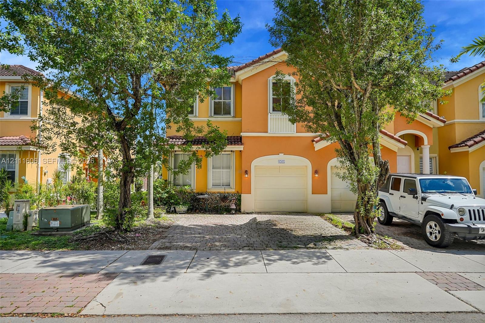 Two-story stucco exterior featuring a tiled roof, arched entryway, multi-paned windows, and a paved two-car garage driveway