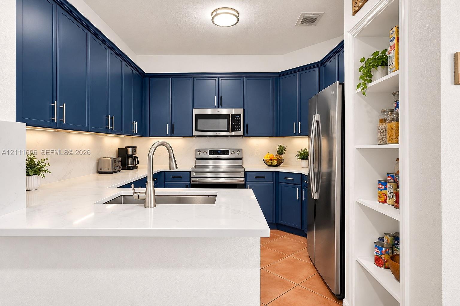 Kitchen featuring navy cabinetry, solid surface countertops, stainless steel appliances, under-cabinet lighting, and built-in shelving Kitchen featuring navy cabinetry, solid surface countertops, stainless steel appliances, under-cabinet lighting, and built-in shelving