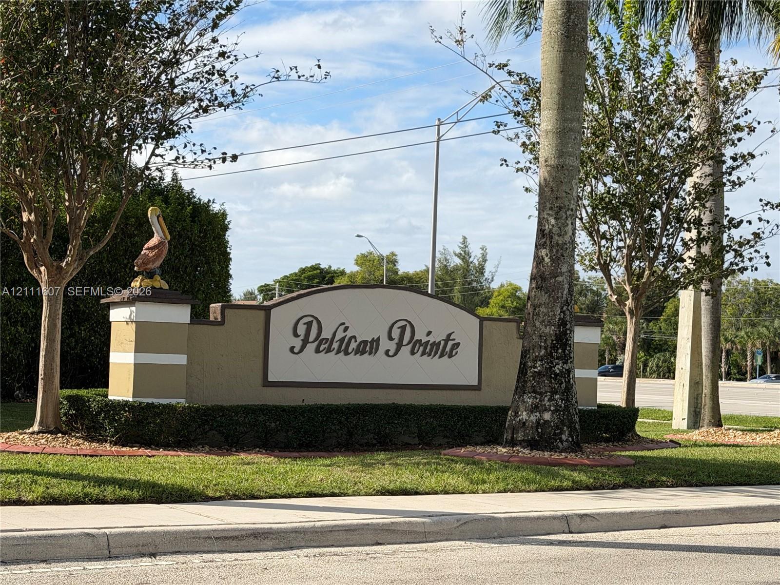 Community entrance monument featuring masonry construction, a decorative pelican finial, and manicured landscaping