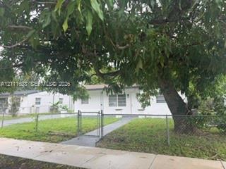 Single-story exterior with light-colored stucco siding, metal-frame windows, and mature canopy tree Single-story exterior with light-colored stucco siding, metal-frame windows, and mature canopy tree