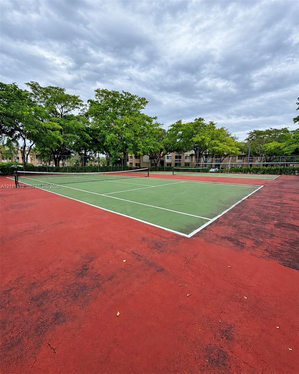 Dual tennis courts featuring perimeter fencing and mature landscaping
