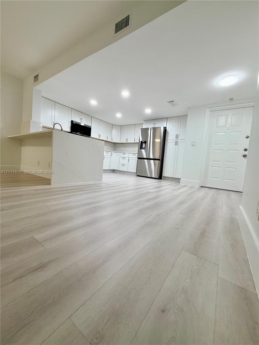 Kitchen featuring white cabinetry, wood-finish flooring, stone-patterned waterfall island, stainless steel refrigerator, and recessed lighting