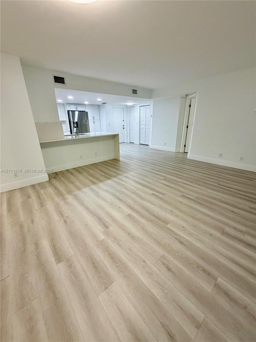 Open-concept interior featuring light-toned wood-finish flooring, a kitchen breakfast bar with solid-surface countertops, white cabinetry, and louvered closet doors