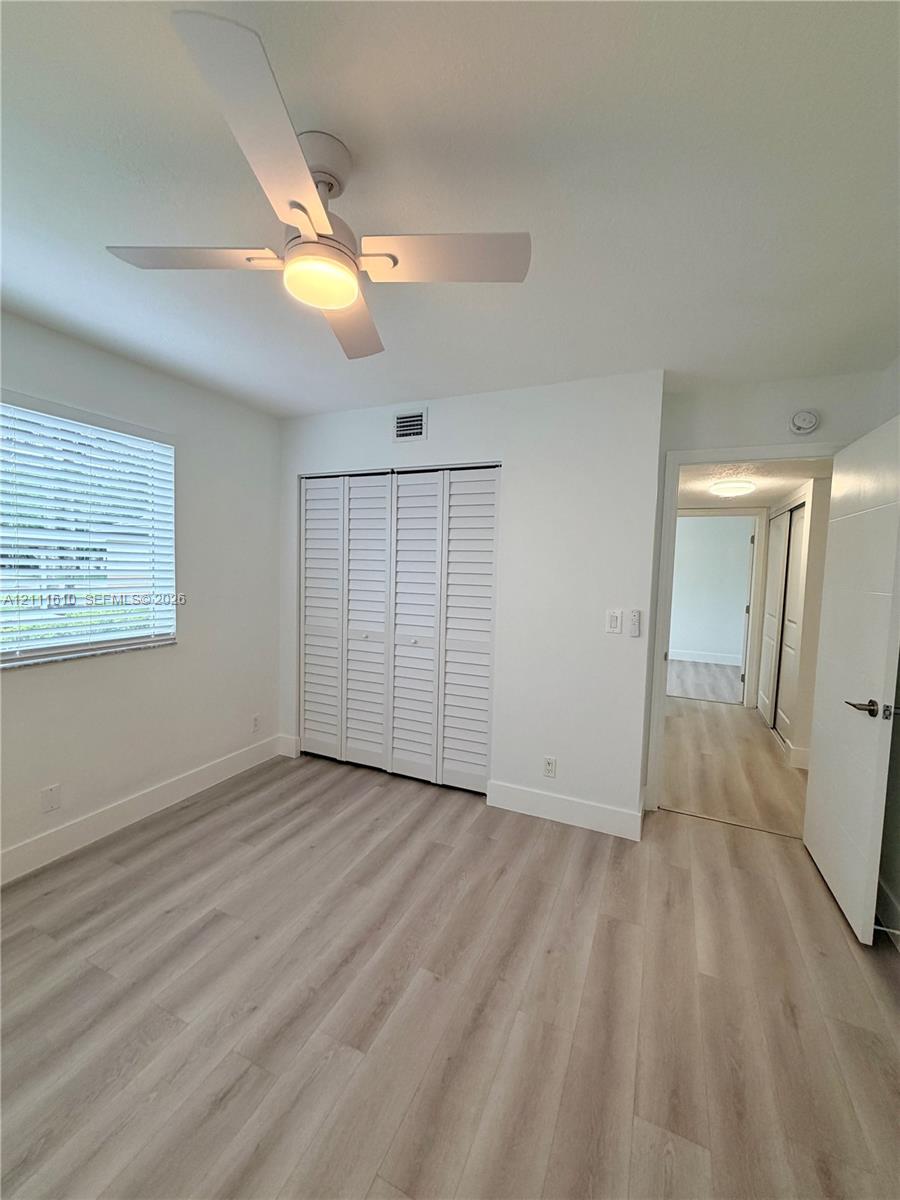 Wood-finish flooring, white louvered closet doors, and an integrated ceiling fan with light fixture