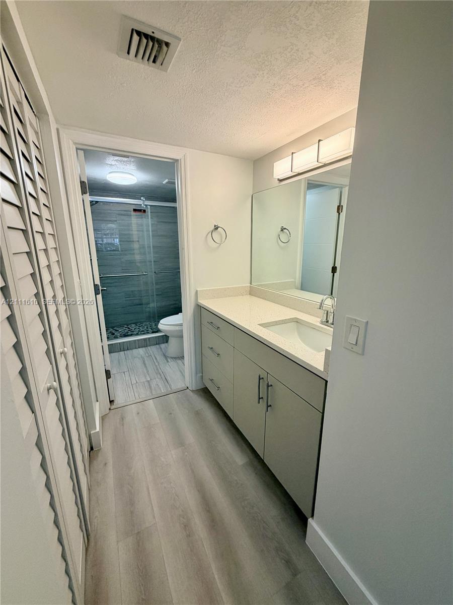 Bathroom featuring a vanity with stone-finish countertop, undermount sink, linear wall-mounted lighting, wood-finish flooring, and a glass-enclosed shower