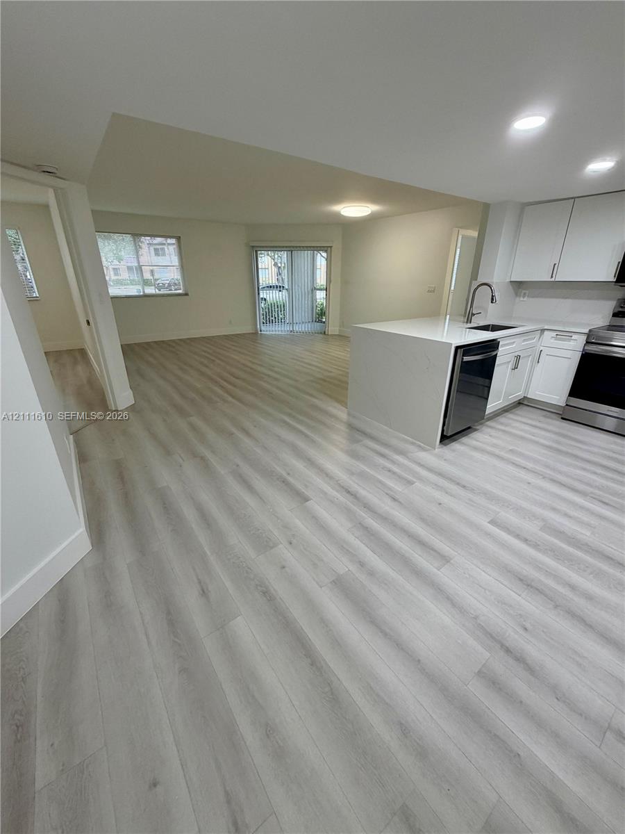 Kitchen featuring white cabinetry, quartz countertops, stainless steel appliances, and a peninsula, complemented by wood-finish flooring