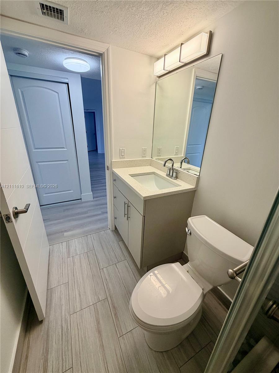 Vanity featuring a stone-surface countertop, rectangular undermount sink, brushed nickel faucet, large wall-mounted mirror, and wood-finish tile flooring