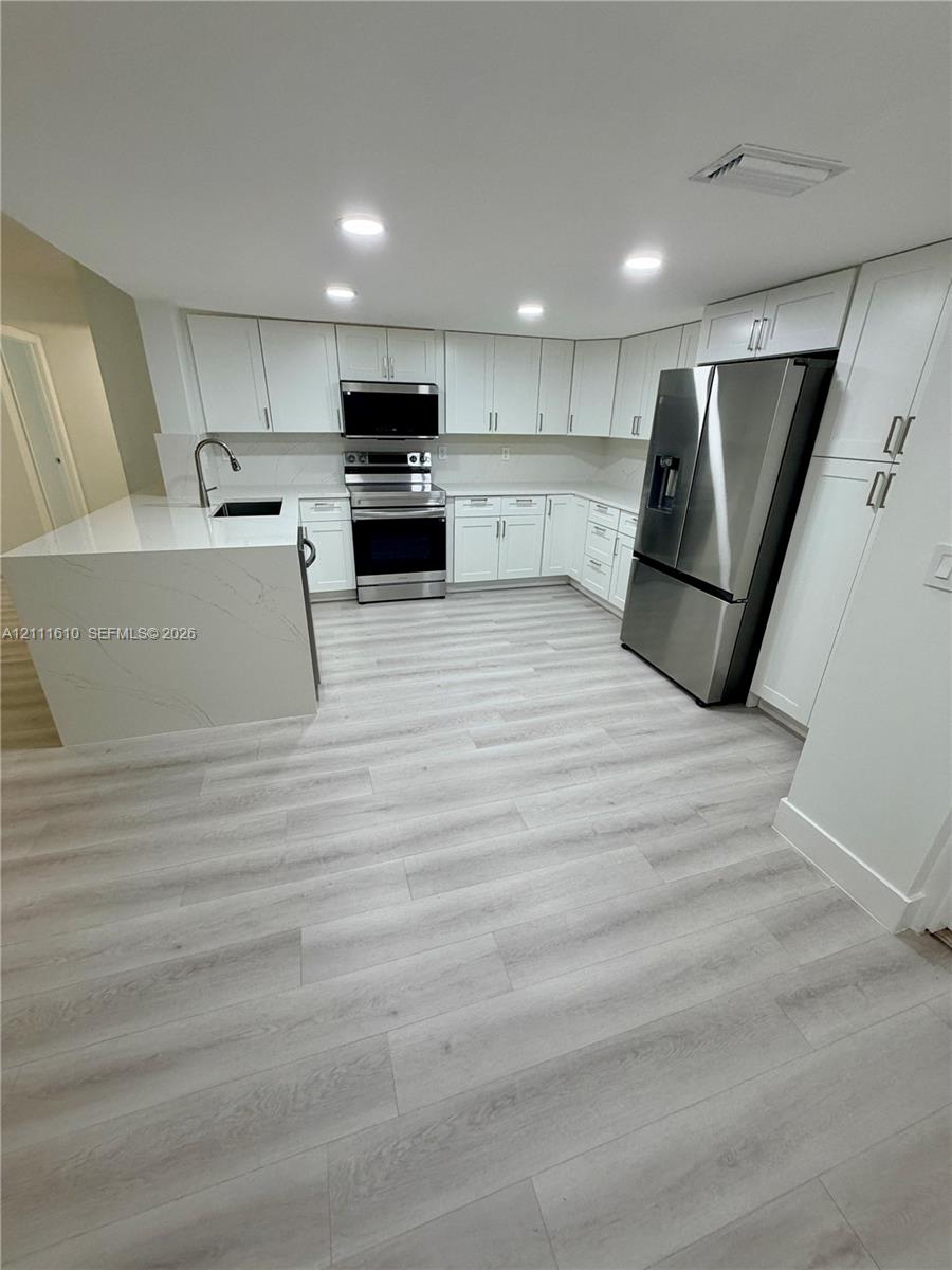 Kitchen featuring white cabinetry, quartz countertops with waterfall edge, wood-finish flooring, and stainless steel appliances