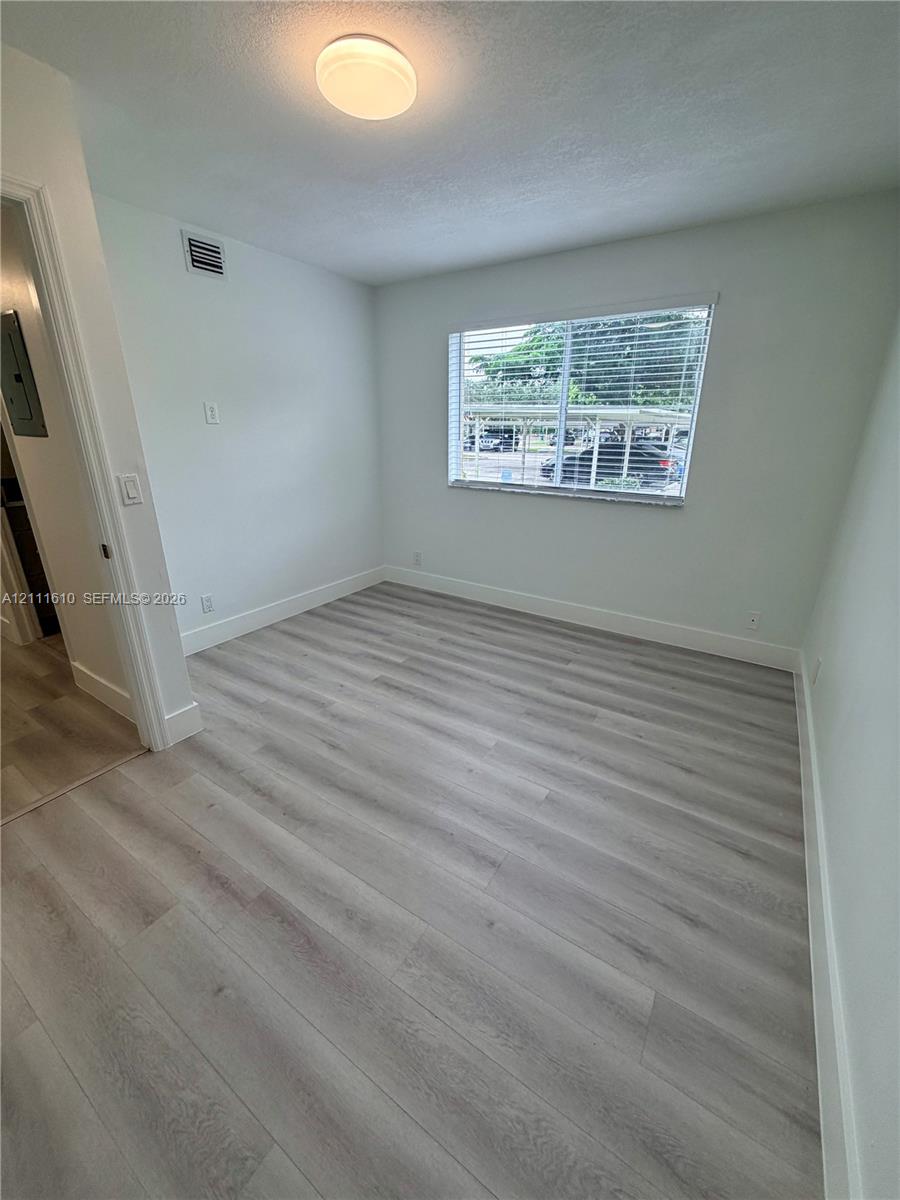 Interior room featuring wood-finish flooring, a single window, and a flush-mount ceiling light fixture
