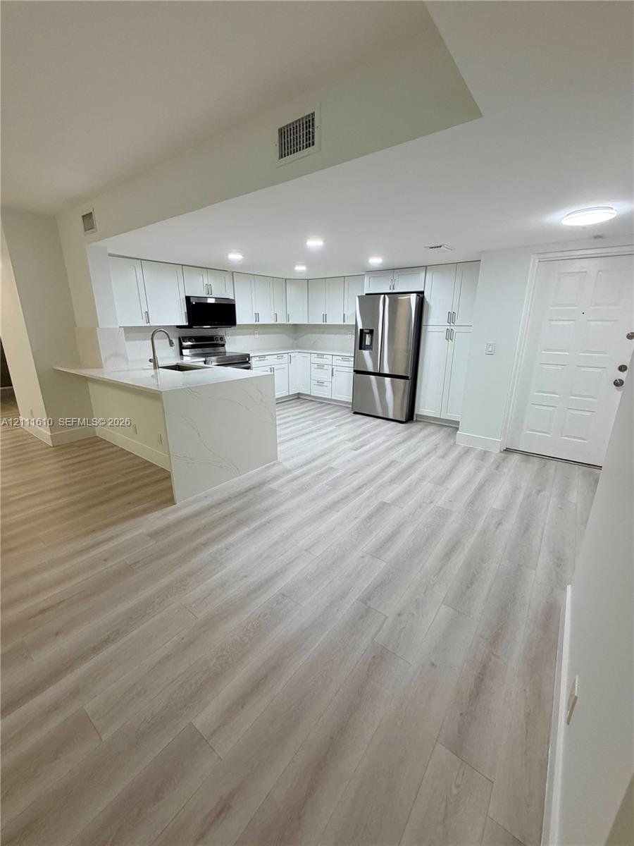 Kitchen featuring white cabinetry, stone-finish countertops, stainless steel appliances, and wood-finish flooring