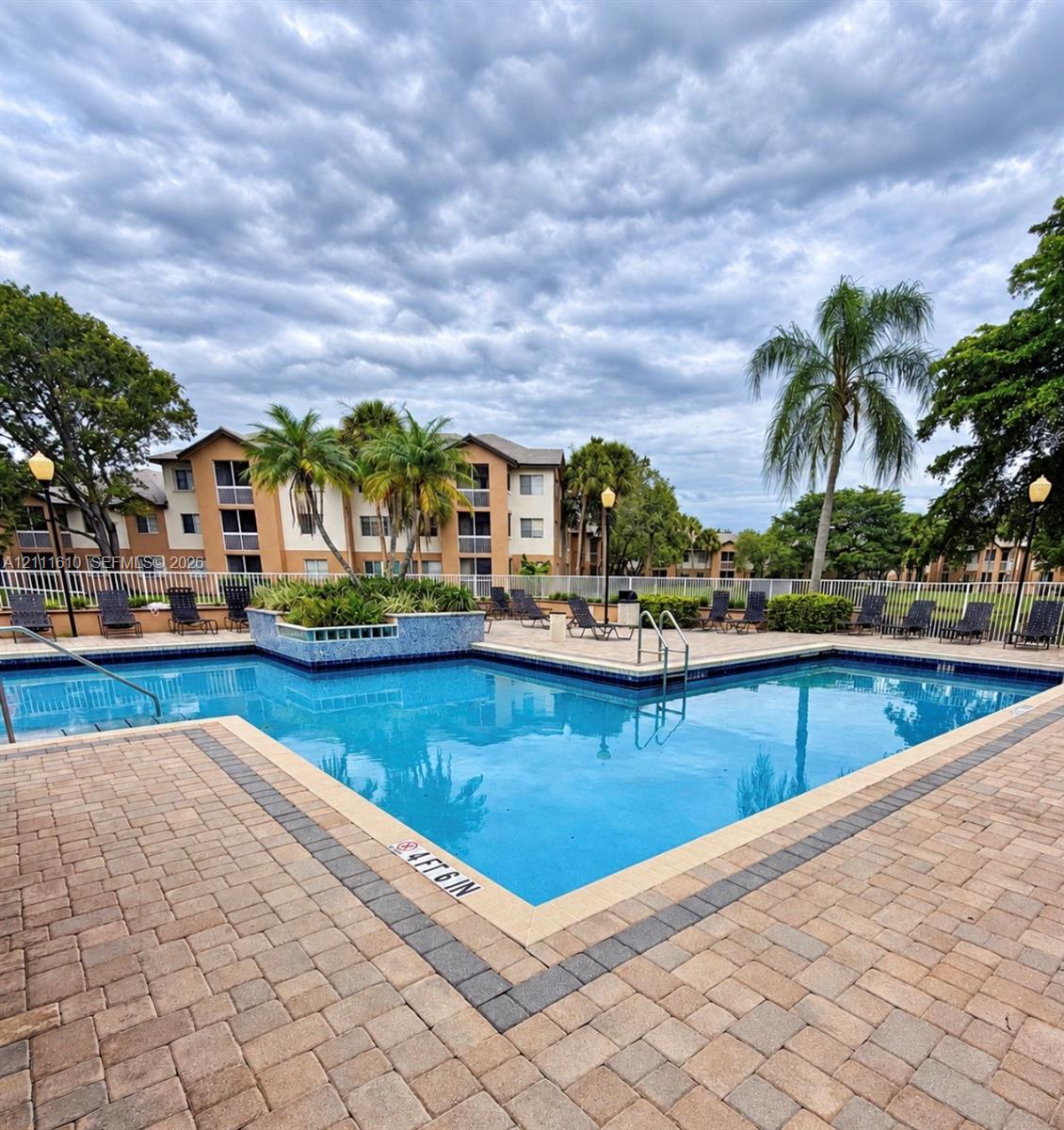 Swimming pool with tiled water line, paver pool deck, metal safety fencing, built-in planter with stone-tile finish, and exterior lighting fixtures
