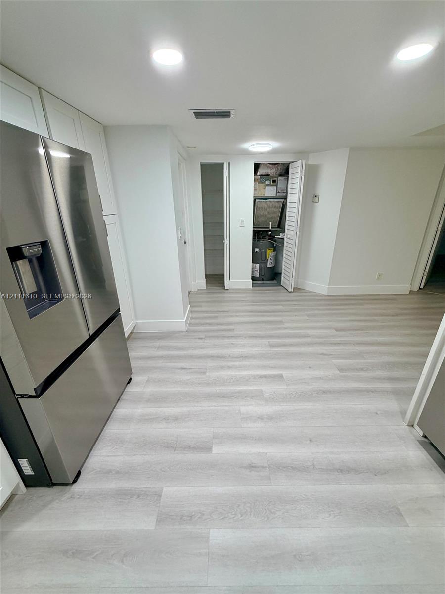 Light-toned wood-finish flooring, stainless steel French door refrigerator, recessed ceiling lighting, and built-in closet storage