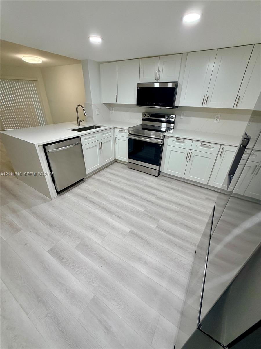 Kitchen featuring white shaker-style cabinetry, white solid-surface countertops, wood-finish flooring, and stainless steel appliances including an over-the-range microwave