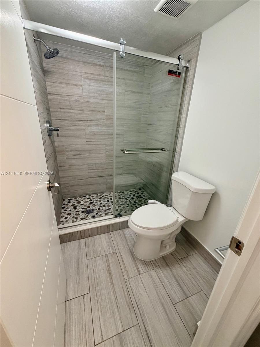 Walk-in shower featuring a sliding glass door, multi-textured stone tile flooring, horizontal wall tiling, and a fixed shower head