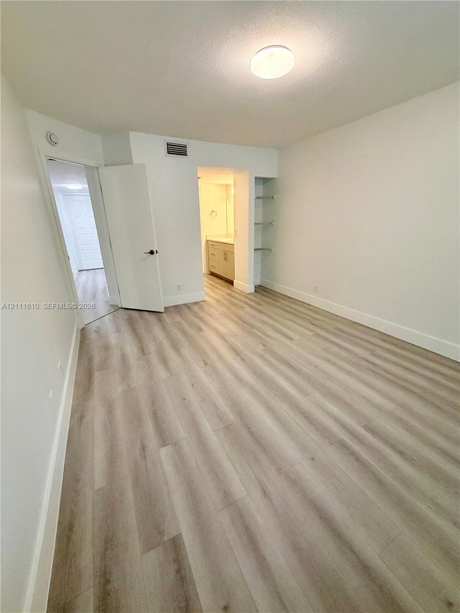 Interior space featuring wood-finish flooring, neutral wall tones, built-in glass shelving, and a flush-mount ceiling light fixture