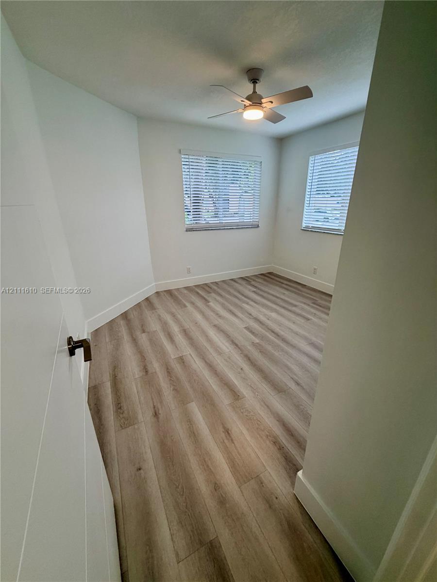 Room featuring wood-finish flooring, dual windows with fitted blinds, and a central ceiling fan with an integrated light fixture