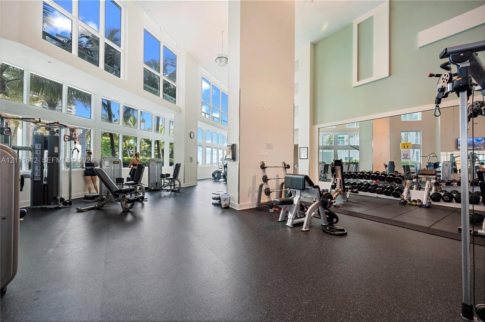 Fitness center featuring double-height ceilings, floor-to-ceiling windows, rubberized flooring, and an expansive wall mirror