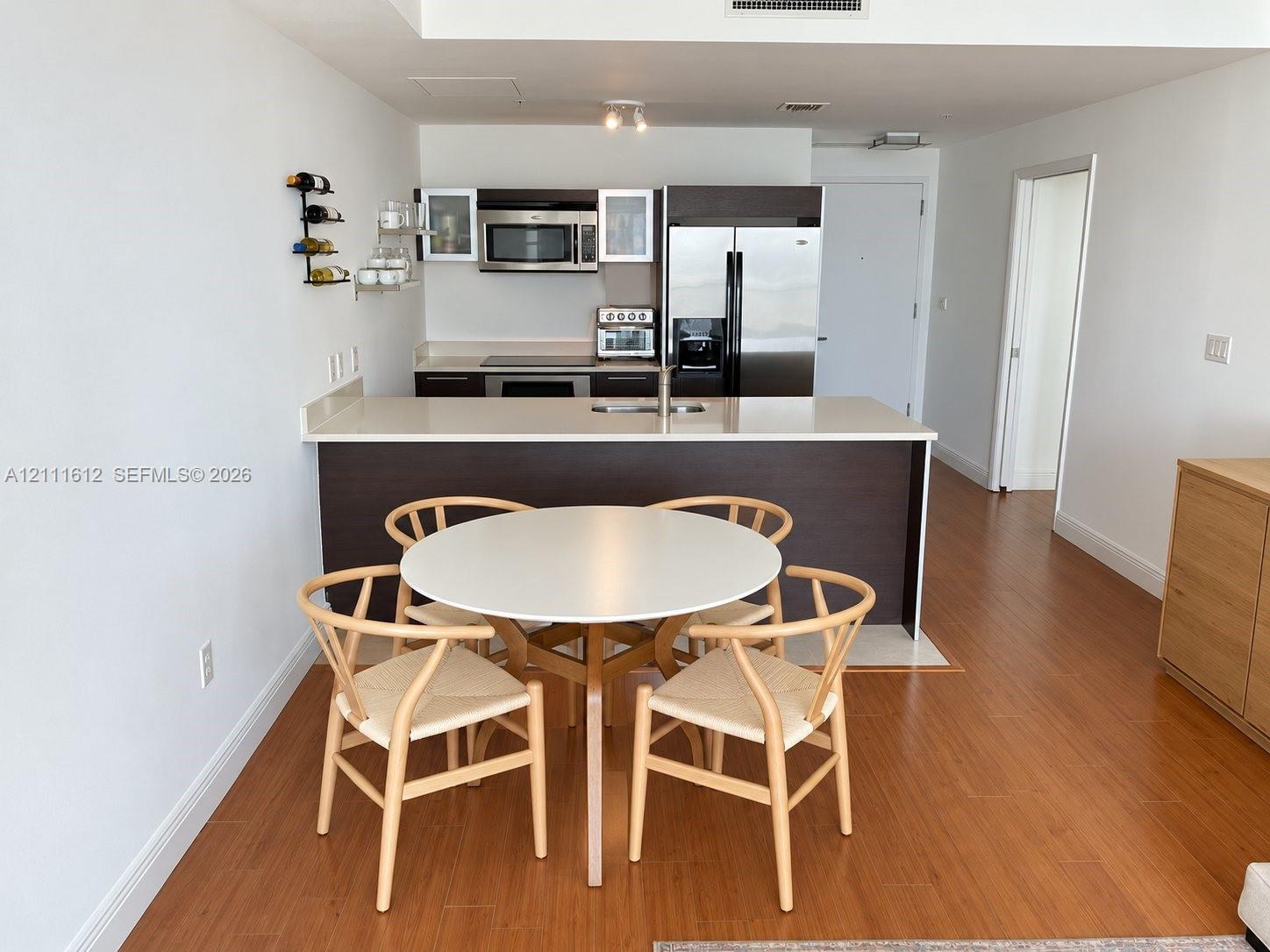 Kitchen featuring a peninsula with solid-surface countertop, dark-finish cabinetry, stainless steel appliances, and wood-finish flooring