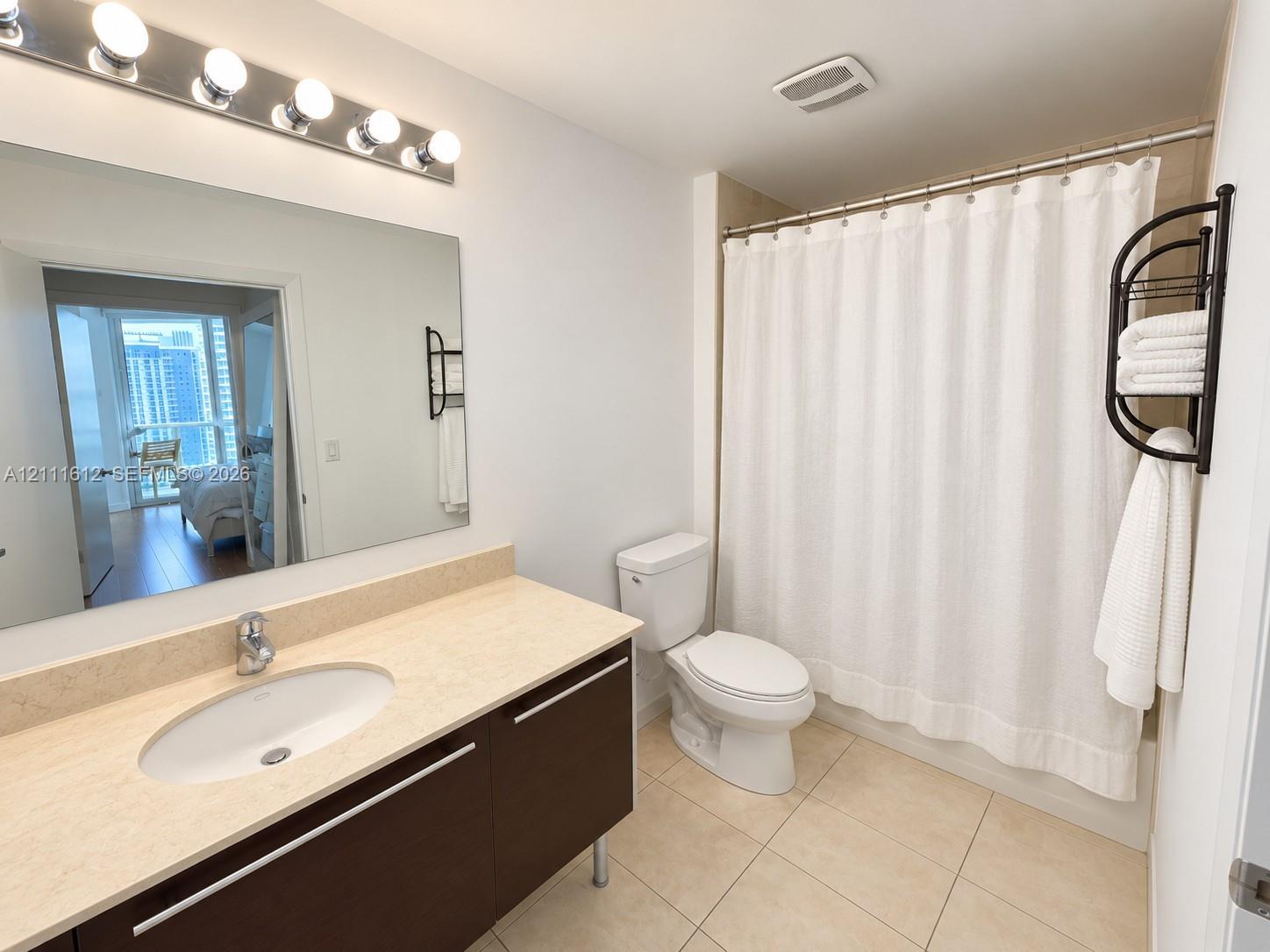 Floating vanity with an integrated sink and light-toned countertop, large wall-mounted mirror, five-bulb vanity light fixture, and tile flooring