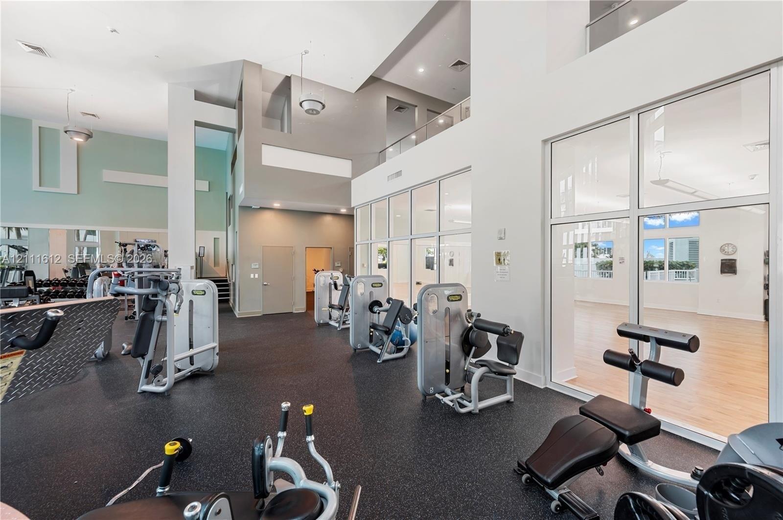 Fitness center featuring high ceilings, rubberized flooring, expansive glass partition walls, and recessed lighting