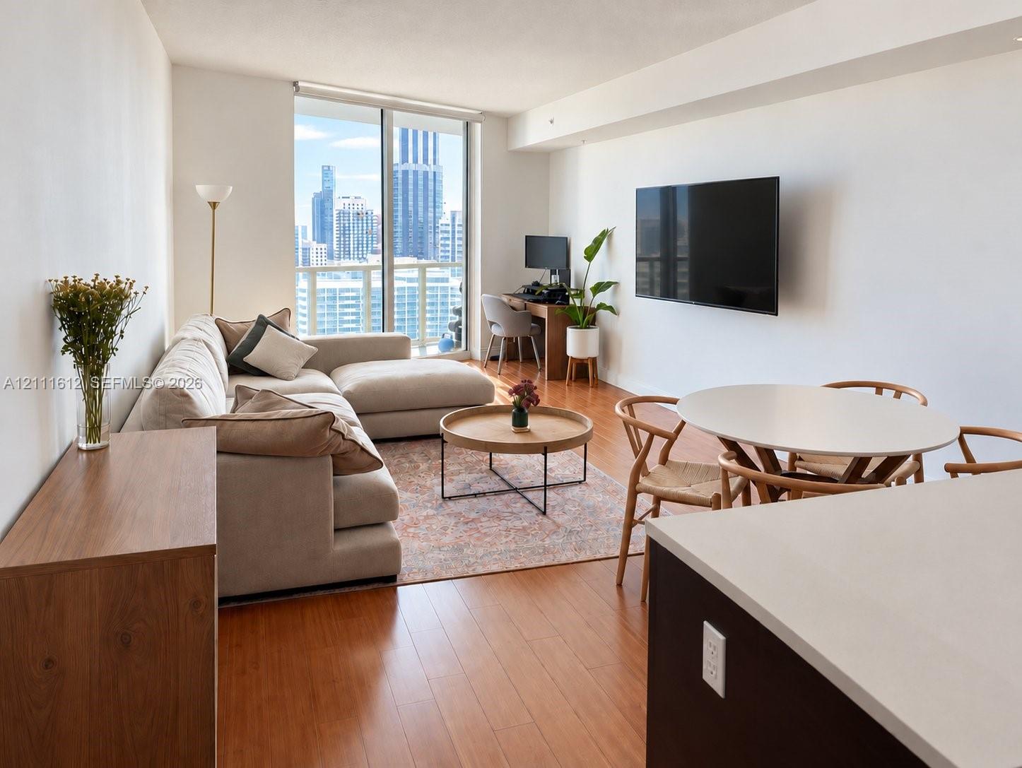 Open-concept living area featuring floor-to-ceiling glass paneling, wood-finish flooring, and a stone-surfaced kitchen peninsula