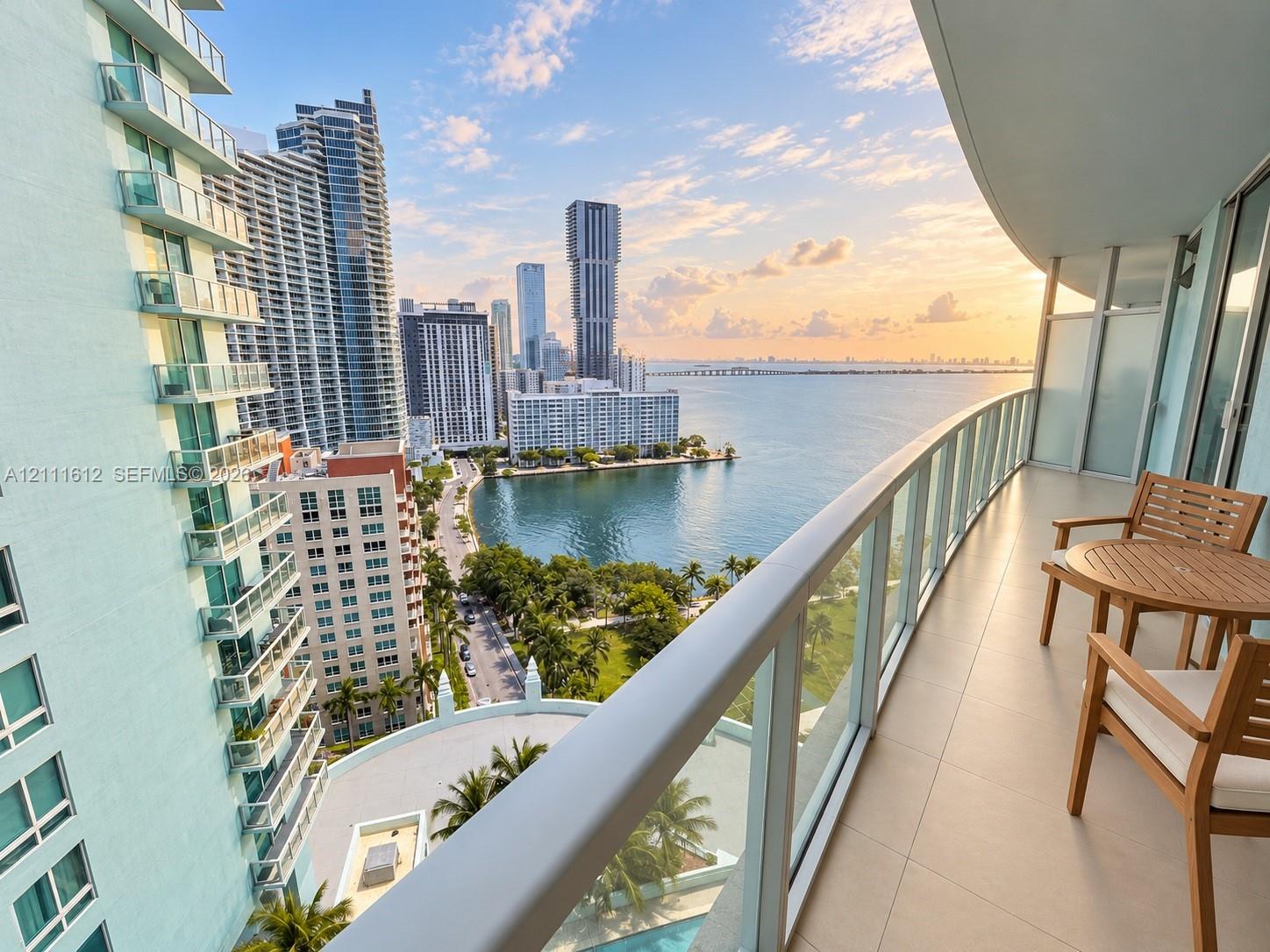 Covered balcony with large-format tile flooring and tempered glass railing, featuring an expansive water and urban skyline backdrop