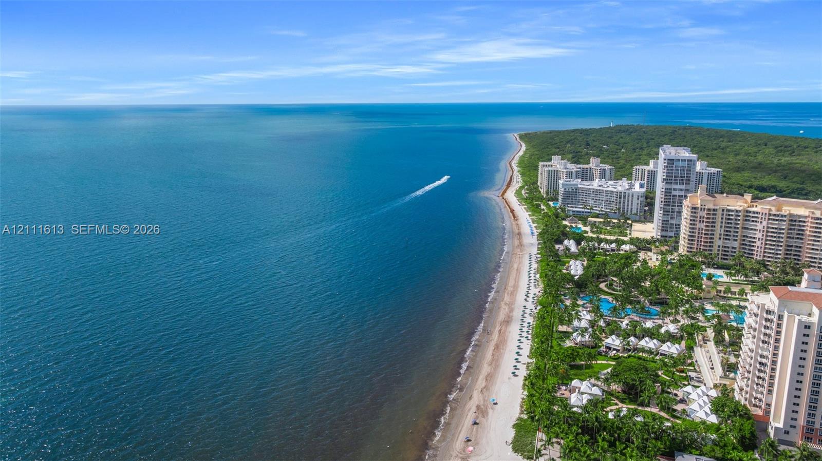 Coastal property featuring direct ocean frontage, expansive sandy beach, and proximity to mid-rise residential structures surrounded by mature tropical landscaping