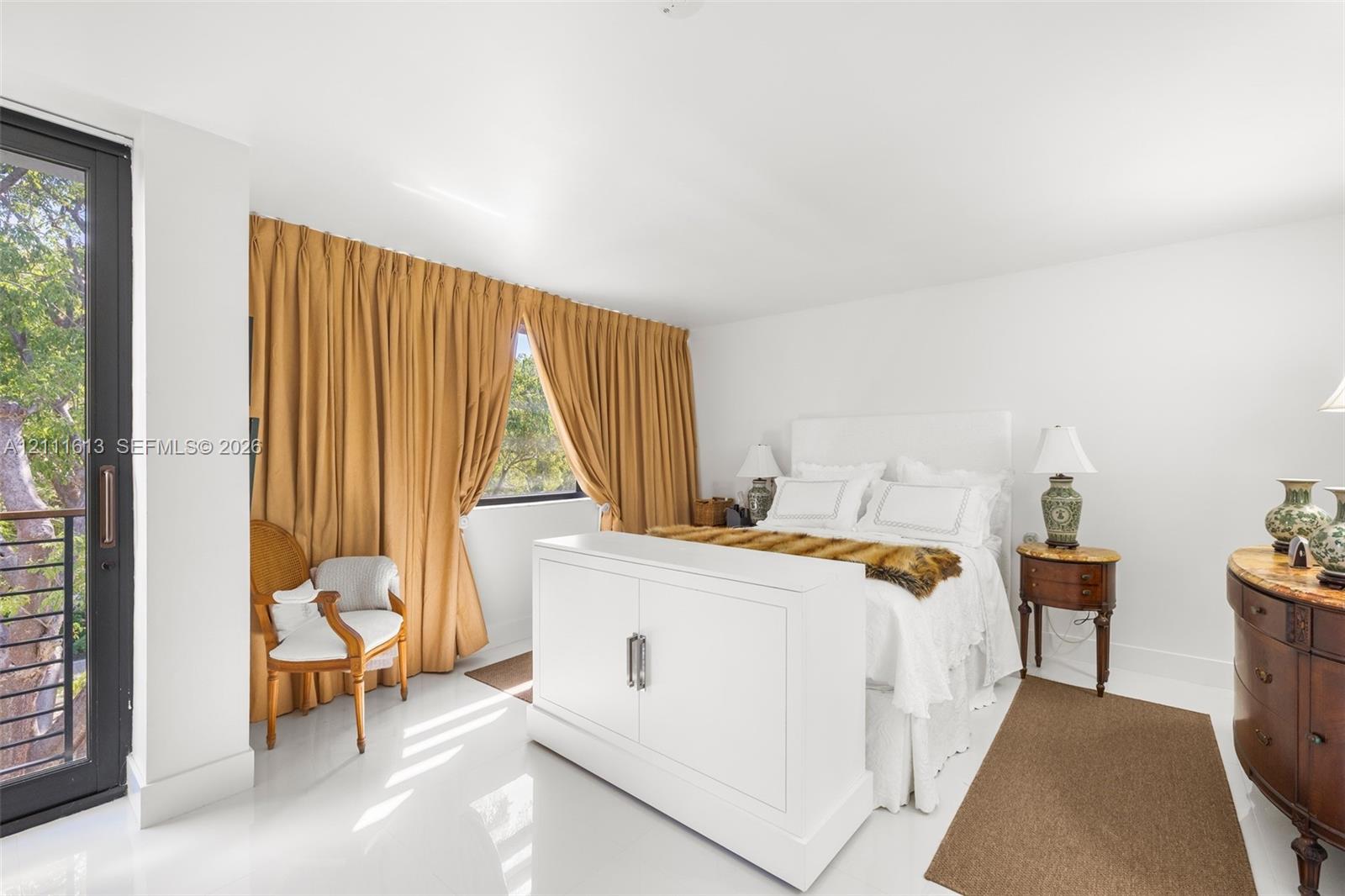 Bright bedroom featuring polished white flooring, floor-to-ceiling drapery, and a dark-framed glass door providing exterior access