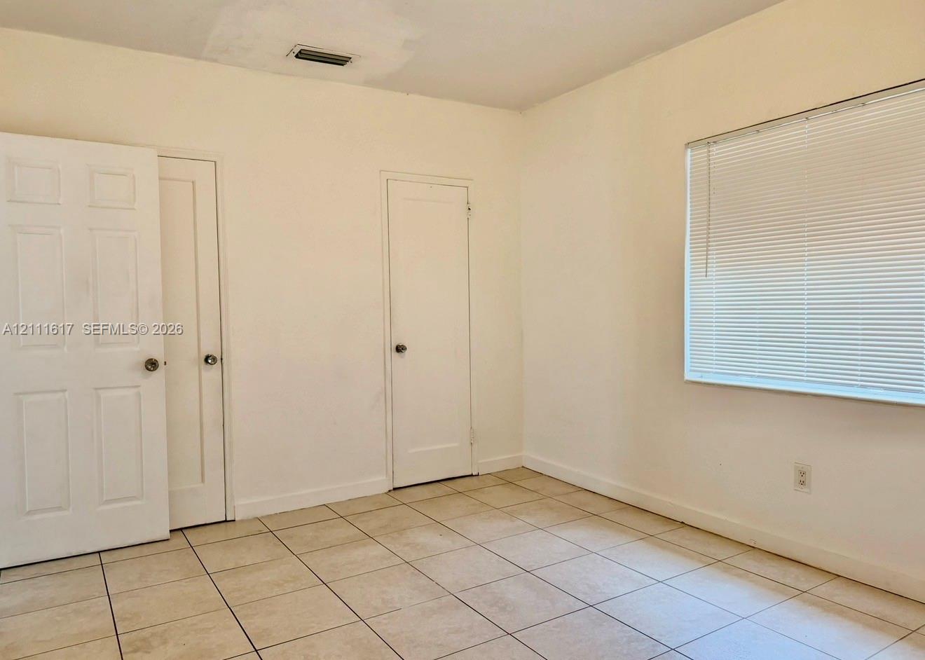 Neutral-toned tile flooring, two solid-core panel doors, and a window fitted with horizontal blinds