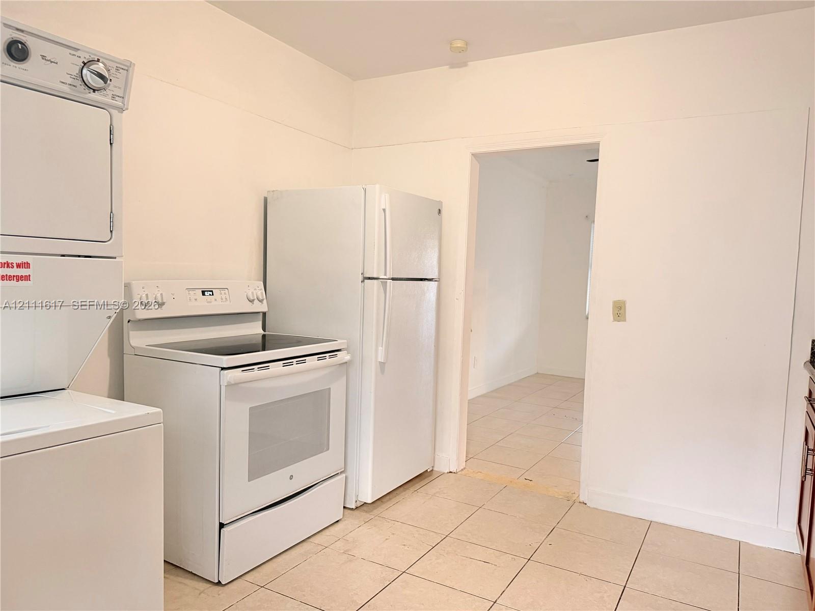 Utility space featuring a stacked washer and dryer unit, white electric range, white refrigerator, and tile flooring